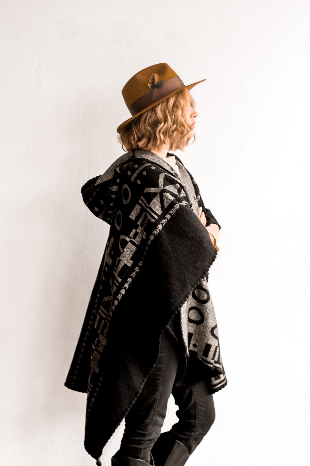 Side view of the woman wearing the OX Black and Grey Poncho without the hood. She paired the poncho with a brown hat, light brown top, and black jeans.
