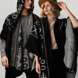 Man wearing the OX Black and Grey Poncho with Hood. He paired it with a grey top and black jeans. He is over a plain grey background. The women next to him wearing the same XO poncho. She paired the poncho with a brown hat, light brown top, and black jeans.
