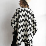 Back of woman modeling the picos ponchos. The pattern features a zig zag pattern across the whole poncho. She wore it with a light brown hat, cream top, and black jeans.