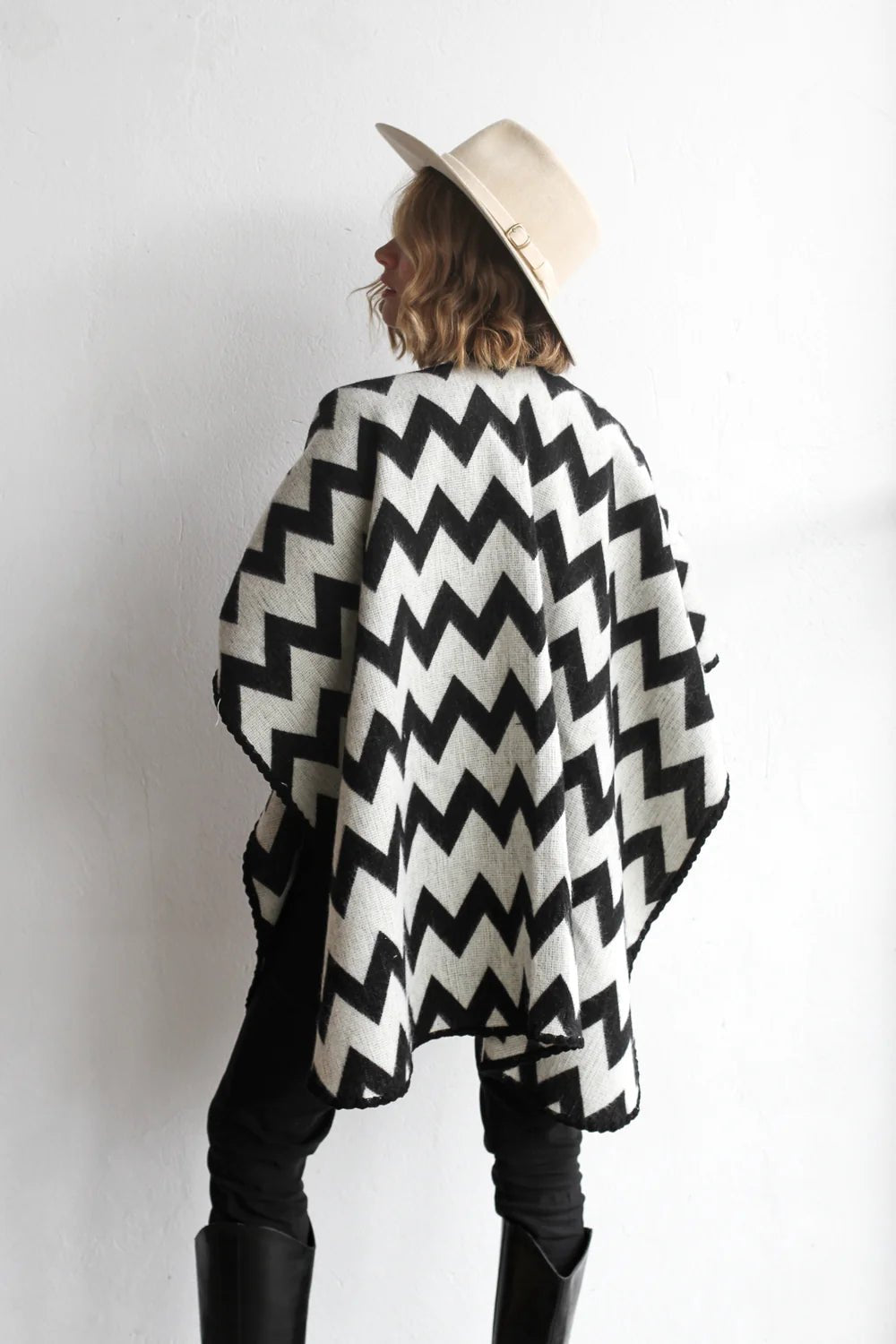 Back of woman modeling the picos ponchos. The pattern features a zig zag pattern across the whole poncho. She wore it with a light brown hat, cream top, and black jeans.