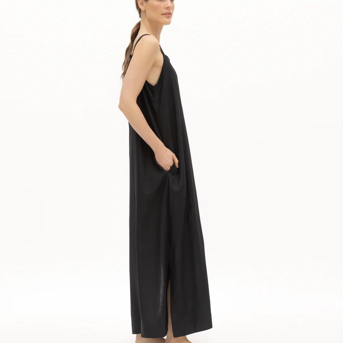 Image of a woman wearing a long dress with pockets and spaghetti straps that was made in Colombia by NAOS. The purpose of this image is to highlight the dress, which is for sale at EVAMAIA boutique in Studio City, CA and online.