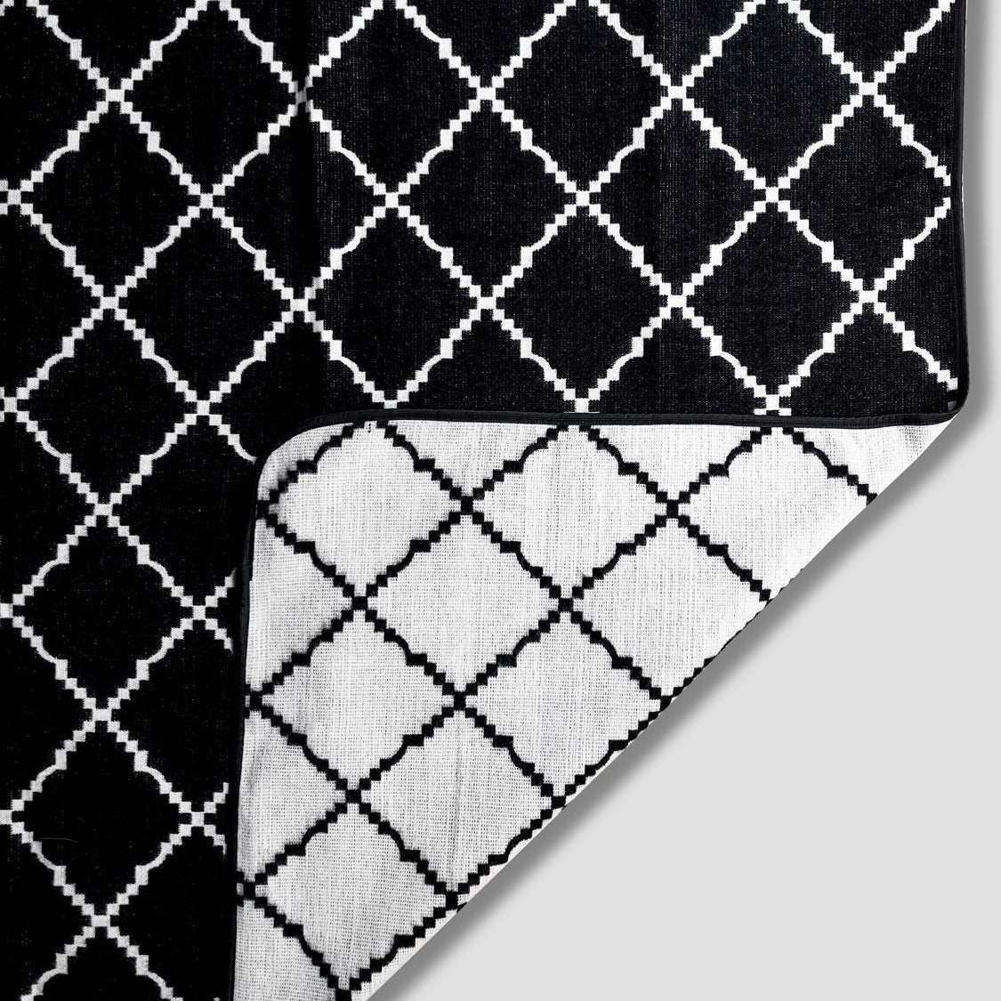 Close up of Royal Reversible Throw Blanket. Image is of  classic black and white crisscross pattern and a corner folded to white and black crisscross pattern.