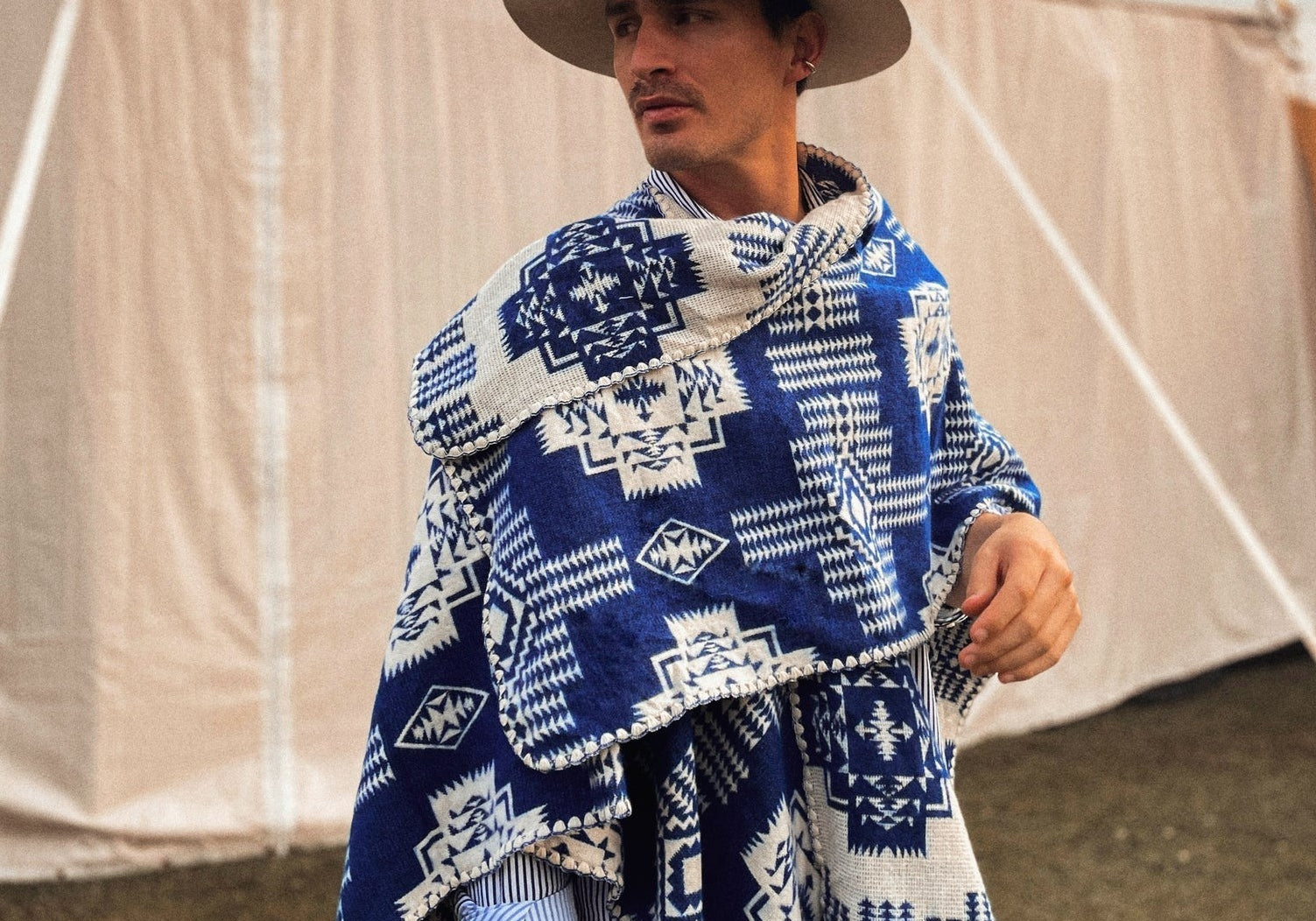 Man wearing the blue sierra poncho. Poncho features a geometric design with tones darker on one side. He is standing outside in front of a tent.