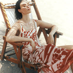 Model laying down on beach chair. She is at the beach relaxing and posing with eyes closed. She is wearing the Sole One Piece Swimsuit in Orange Mare with its matching sarong. 