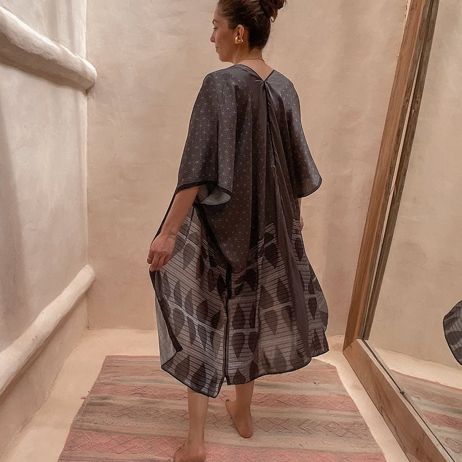 Model wearing the Tokyo Kimono by PLISSÉ. She is modeling the back of the kimono. The pattern of the kimono is a geometric pattern, all in different tones of grey.