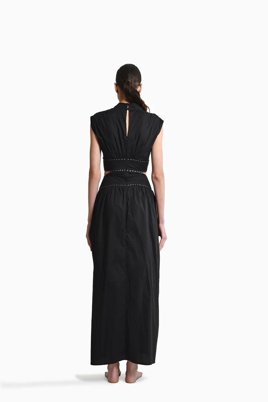 Back of Model wearing Toya Maxi Dress with Side Cutouts, mockneck and gold stitching around waist on plain white background