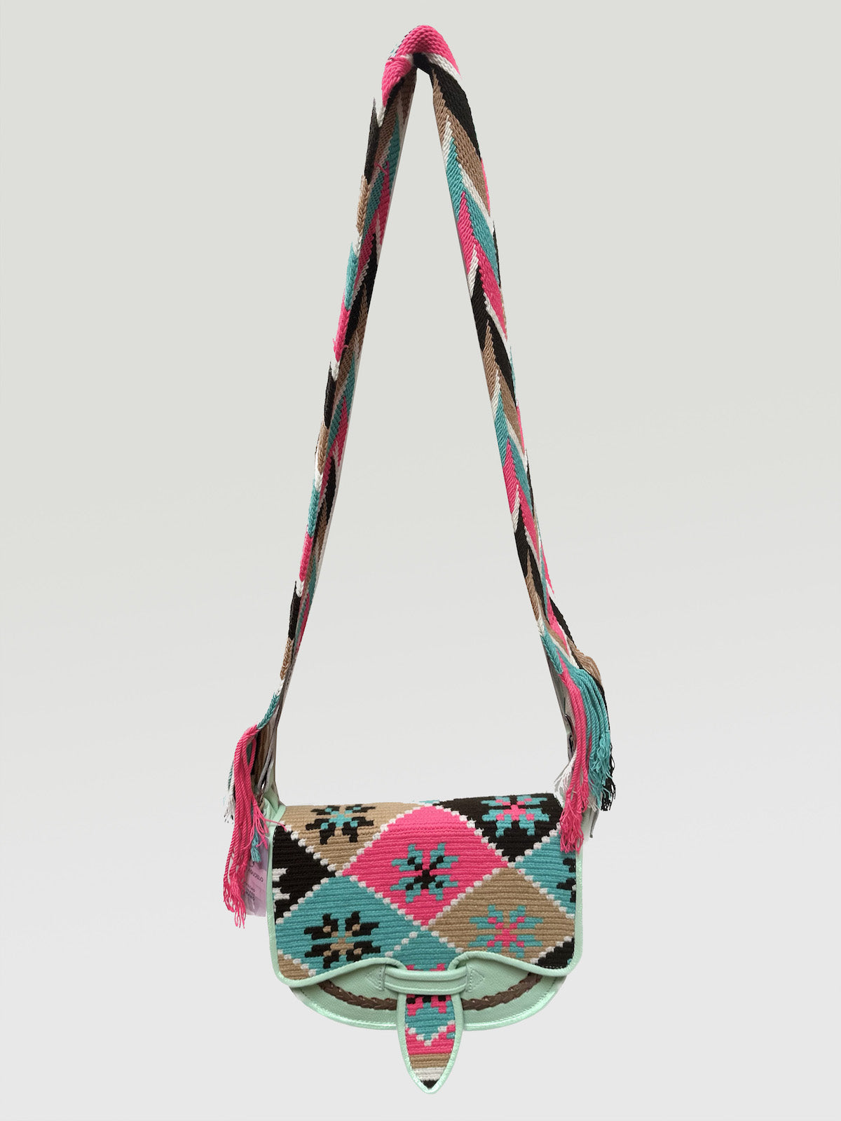 A multicolored floral patterned Wayuu crossbody carriel  bag with a pink strap and fringe detailing.