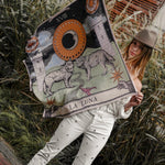 Model holding up the Zodiac Moon Scarf. Scene has brick flooring, plants behind her.