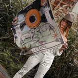 Model holding up the Zodiac Moon Scarf. Scene has brick flooring, plants behind her.