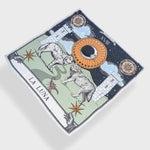 Zodiac Moon Scarf by Plissé. Image includes the night sky full of stars, towers, and playful elements like the wolves and stars. Scarf is floating on white background.