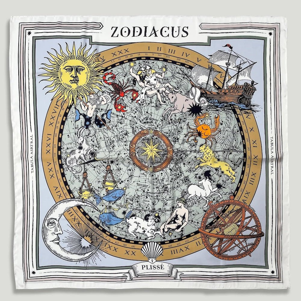 Zodiac Scarf for all zodiac signs made by Plissé. Image of all zodiac symbols, like the twins, bull, crab, lion, archer, etc. It is on top of a astrological background. Details like a orange ecliptic, yellow sun, and white moon. The scarf is white with brown details displayed on plain white background.