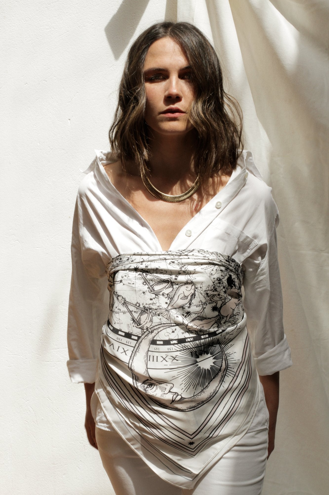 Woman modeling white zodiac scarf wrapped as Classic Bandana Top over a white long button up shirt.