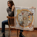 Man holding up brown zodiac scarf while sitting on chair backwards