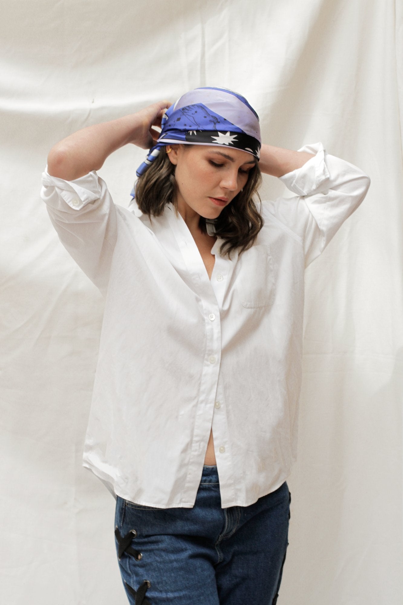 Model wearing white 3/4 sleeve top, blue jeans, wearing the Zodiac Scarf for Aquarius wrapped on head. She is standing on a plain white background.