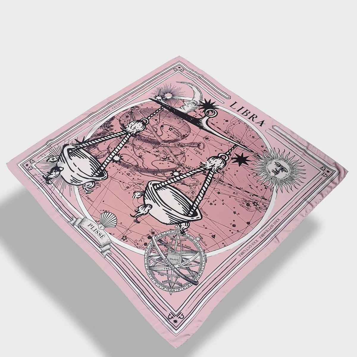 Zodiac Scarf for Libra made by Plissé. Image of scales. It is on top of a astrological background. Details like a white ecliptic, sun, and moon. The scarf is pink with white details floating on plain background.