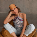 Woman modeling Zodiac Scarf for Sagittarius as a top tied to gold collar necklace. She is criss crossed on couch.
