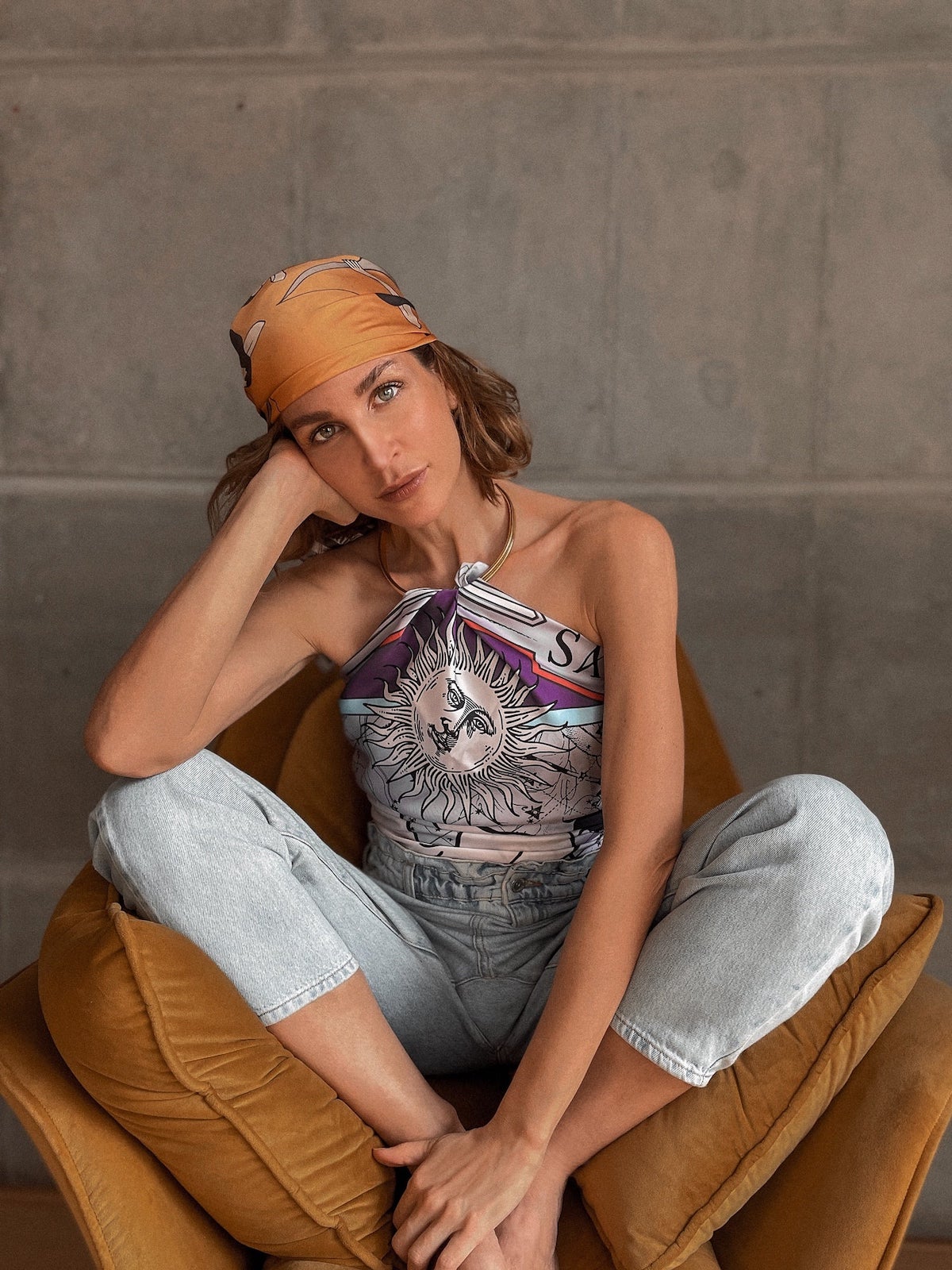 Woman modeling Zodiac Scarf for Sagittarius as a top tied to gold collar necklace. She is criss crossed on couch.