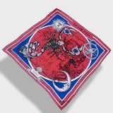Red scorpio scarf by Plissé. Image of a scorpion, with sun and moon on corners. The scarf is pictured on plain white background.