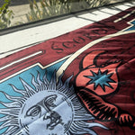 Close up of burgundy scorpio scarf by Plissé. Image of a scorpion, with sun and moon on corners. The scarf is pictured laid out on window of EVAMAIA.