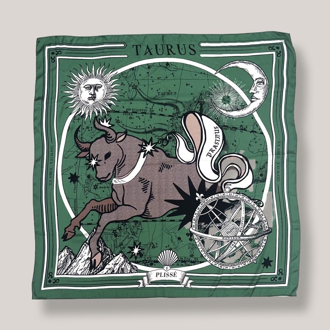 Zodiac Scarf for Taurus made by Plissé. Image of a bull. It is on top of a astrological background. Details of an ecliptic, sun, moon, and mountain range. The scarf is a dark green color displayed on top of a plain white background.
